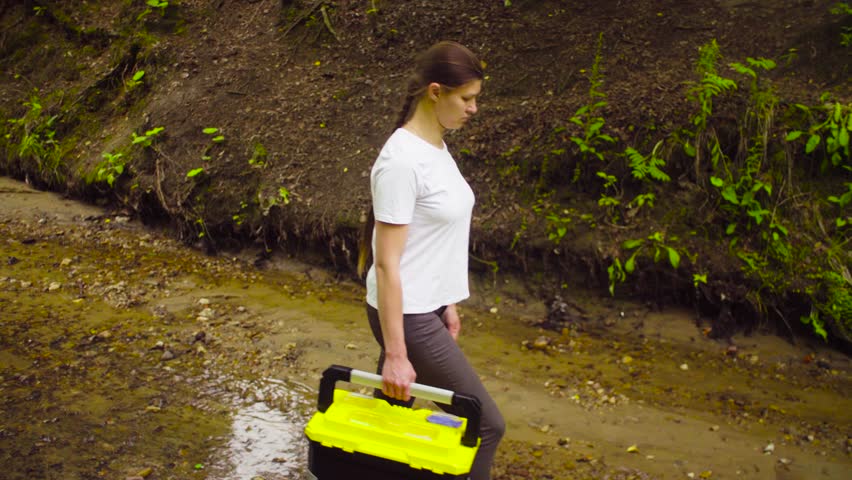 Follow shot. The woman scientist environmentalist with the tool box in her hand going to the place of research in the creek. Side view. Royalty-Free Stock Footage #1015023604
