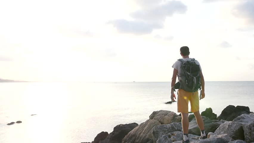 A man gets the joy of traveling, standing on the rocks on the seashore will raise his hands up. slow motion. 1920x1080. full hd