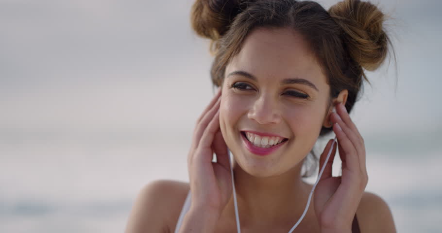 Close up  portrait of happy young woman puts on earphones smiling enjoying listening to music on seaside beach slow motion | Shutterstock HD Video #1015030081