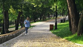 Carefree blonde woman student walking with book in park and looking away