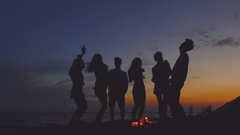 Group of people dancing at the beach near the bonfire. Slow motion.