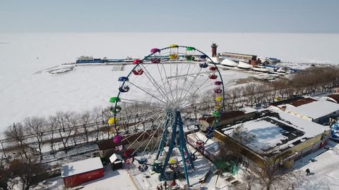 Aerial approach Sports waterfront promenade Ferris Wheel colorful high entertainment. Coastal sea frozen white Blue sky horizon. Tourist attraction Travel. Winter snow field cold Sunny. Helicopter 4k Vídeo Stock