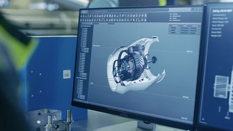 Close-up Shot of the 3D CAD Model of the Engine Shown on Computer Screen. In the Background Manufacturing Factory with People Working. 