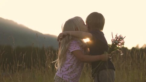 Little girl in the field at sunset, kisses the boy for what he gave her flowers