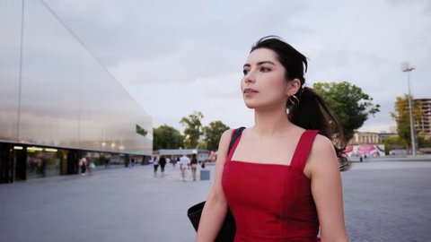 Attractive young brunette girl in red dress walking on summer street. Slow motion