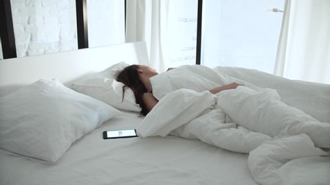 Alarm Clock On Phone. Tired Woman Waking Up In Bed At Bedroom