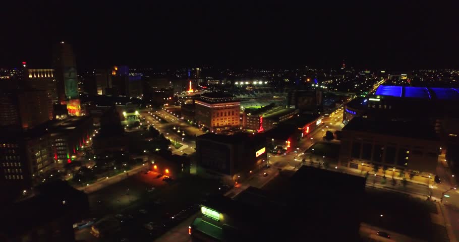Aerial at night of Detroit Michigan downtown. You can see office buildings and cars driving on the street as the street lights glow in the night.