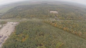 Quadrocopter, flying over the autumn forest. Autumn cloudy day. Video shooting from a bird's-eye view. Quadrocopter flies over the forest, dirt roads and construction sites.

