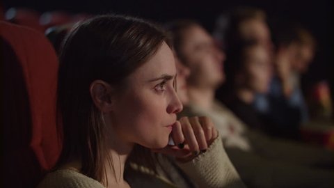 Concentrated girl watching thrilling movie at cinema. Young woman watching movie in movie theater. Pretty girl watching exciting movie in cinema. Enjoy cinema concept