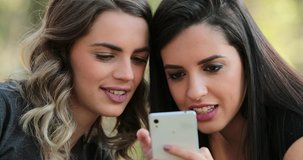 Authentic friends laughing together outdoors checking cellphone. Close-up Girlfriends looking and holding smartphone together