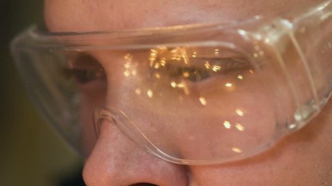 A man at a 4K plant close-up welding. Sparks from welding are reflected in the glasses. A person in close-up glasses makes welding. The guy works as a welder at the enterprise. Reflections in glasses.