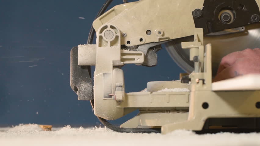 Worker in overalls on blue background closeup slow motion wood item on electric saw. stream of sawdust from machine tool when processing tree. When processing bar, large amount of chips is deposited.