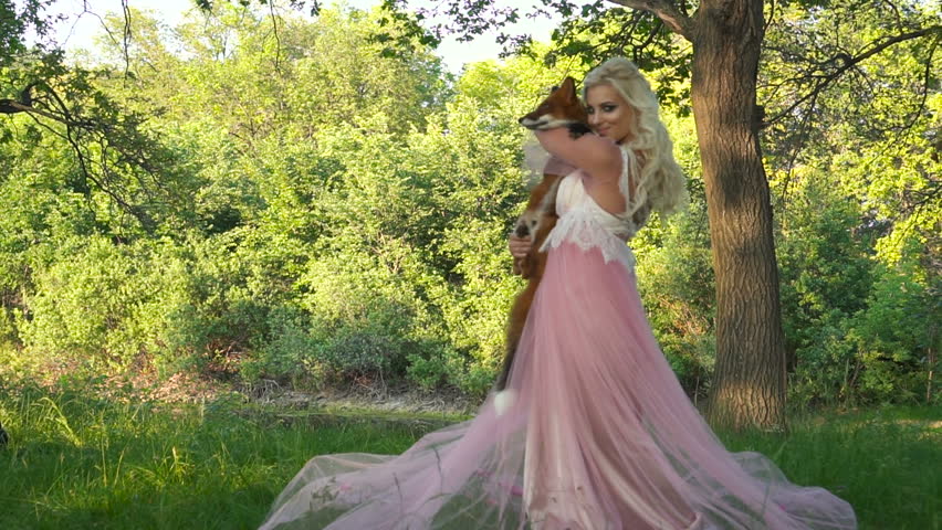 happy girl holding a fox in her arms and smiling at her. It is near the blooming trees, in the spring park.