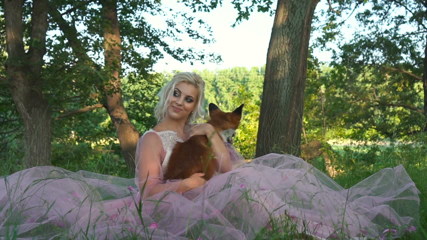 Portrait beautiful woman holding red fox in her hands and smiling. Attractive blonde with foxes in her arms. Close up young woman holding a cat in forest. Fox sits on hands sexy girl