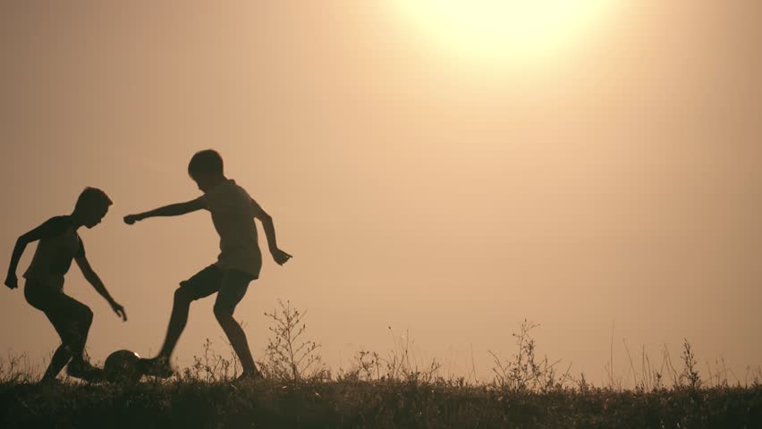 Two boys playing soccer at sunset. Silhouette of children playing with a ball at sunset. The concept of a happy family. Silhouette of children with a soccer ball. children playing in park at sunset Royalty-Free Stock Footage #1015077739