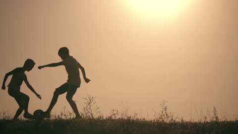 Two boys playing soccer at sunset. Silhouette of children playing with a ball at sunset. The concept of a happy family. Silhouette of children with a soccer ball. children playing in park at sunset