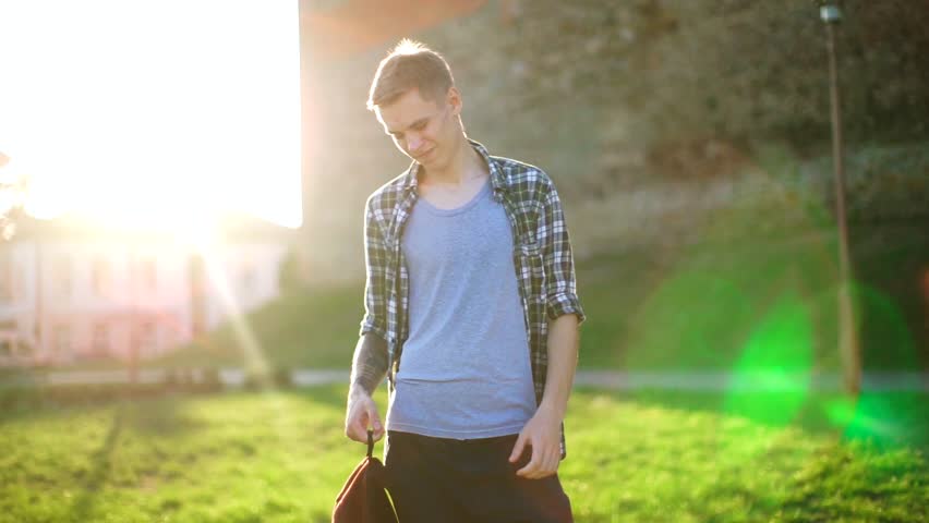Handsome guy smiling in the sun.Guy model wears a backpack on his shoulders. Cute man in a plaid shirt smiling at the camera and straightens her hair. Beautiful model smiling at sunset.