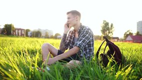 Handsome guy taking a selfie. The student is sitting on the grass and talking on video. A young man smiles and takes a selfie. Cute guy sitting with a phone at sunset.
