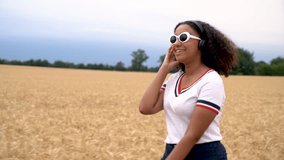 Slow motion HD tracking video of beautiful mixed race African American girl teenager young woman wearing a white t-shirt and sunglasses listening to music on her cell phone and wireless headphones 
