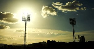a timelapse of the sun going down behind a light tower from a baseball field