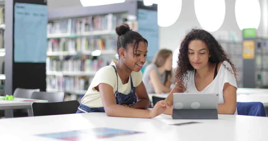 High school students studying together in a library with a digital tablet