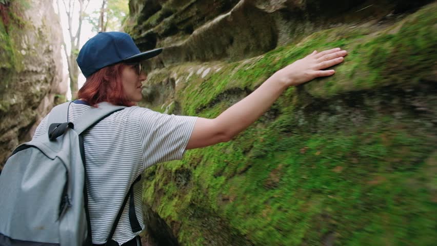 Girls touching with hands a big green stone covered with moss in the forest during walking