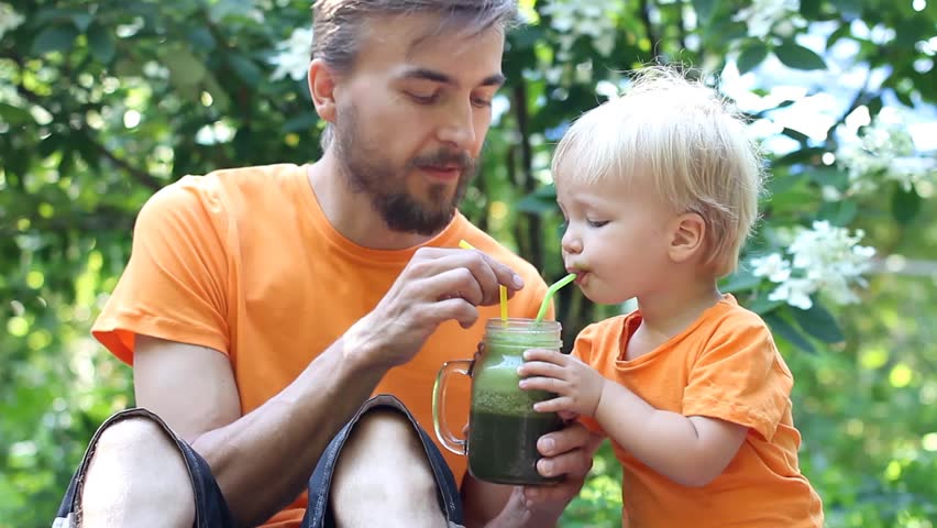 Father and his toddler son drinks fresh green smoothie from one jar and two coctail straws  outdoor. Healthy food or vegan concept. Royalty-Free Stock Footage #1015108426