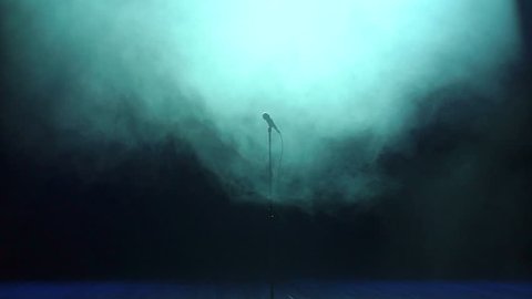 Microphone on stage against a black background with blue lighting. Microphone in a smoke on a dark background. Music instrument concept.