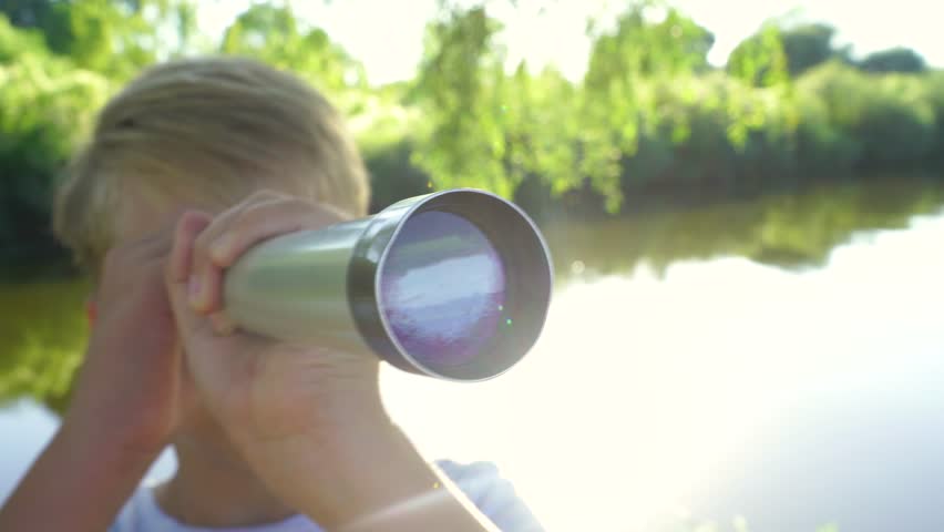 Close up portrait of happy and curious little boy looking through telescope outside. Discovery, exploration and curiosity consept. Real time 4k video footage.