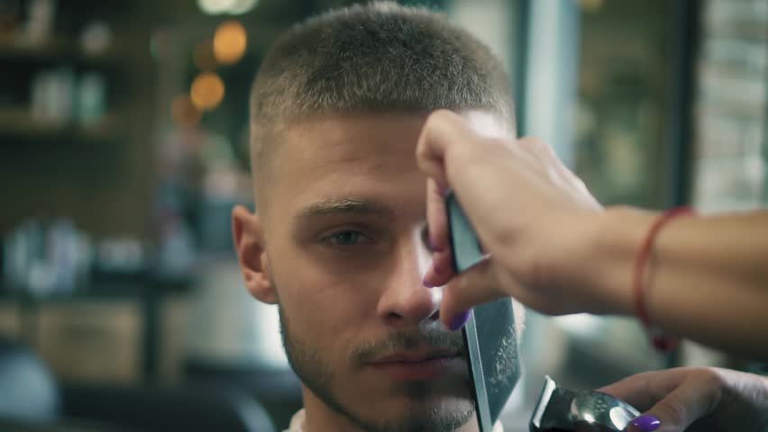 Female barber hand shaving beard with clipper at barber shop. Styling beard with electric trimmer in hair salon. Slow motion. | Shutterstock HD Video #1015125385