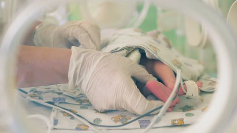 One nurse touches a newborn baby, looking at his feet.