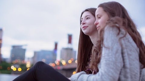 Time lapse shot of friends listening music while sitting against cloudy sky in city during sunset