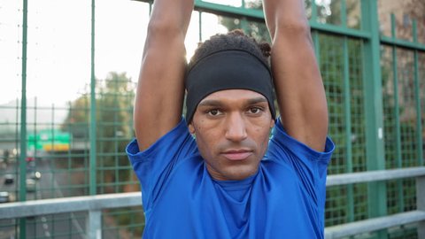 Handheld close-up portrait of male athlete exercising on bridge against fence