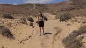 Young cheerful blonde girl walking between sand dunes and coming to kiss the camera in Canary Islands of Spain