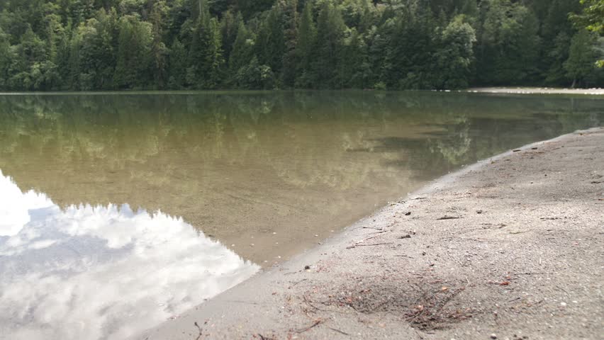 Close Up of Woman Rolling Up Pants and Walking into Lake with Beautiful Reflections of the Surrounding Trees. Latina Middle Aged Female is Alone and Independent. British Columbia, Canada
