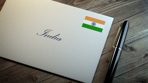Country name written on a card or envelope in cursive font with a sleek pen on a wooden table surface under beautiful classy light. Stamp in the corner shows the flag of India
