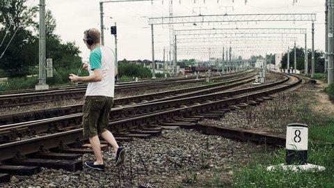 man listening to music on headphones and inattentively crosses a railway or railroad, life threatening