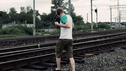man listening to music on earphones and inattentively crosses a railway or railroad, life threatening