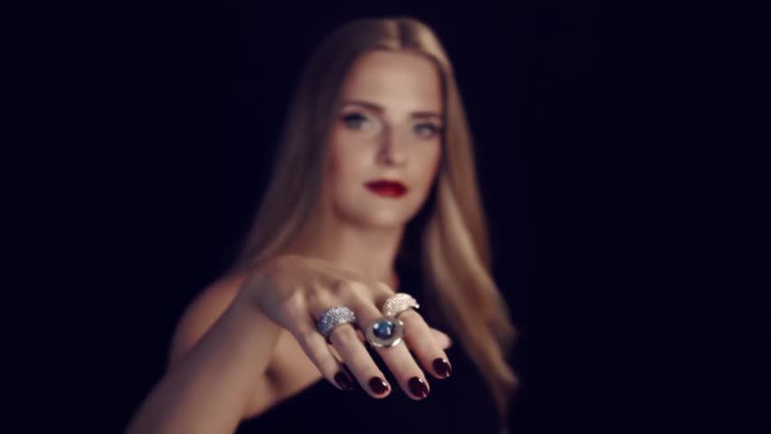 Rings on each finger. Beautiful girl demonstrates the rings in front of the camera on her arm. Female hand with rings on fingers. Black background in the studio.