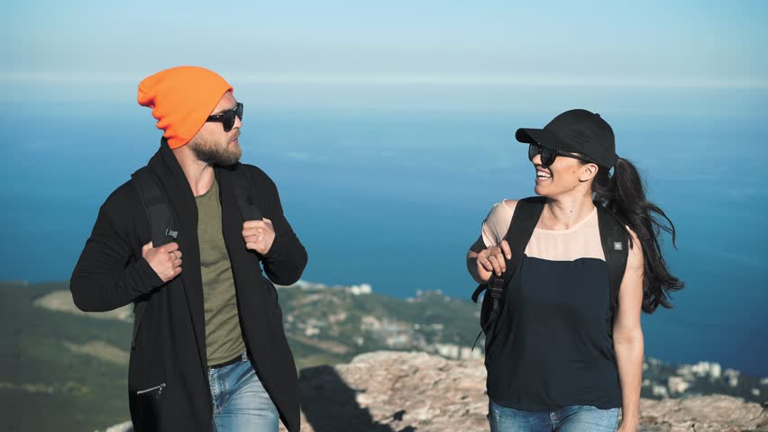 Tourist couple in hat and sunglasses leaving cliff edge smiling talking steadicam establish shot