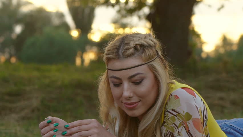 portrait of a young blonde woman with hippies. a woman with braided hair lies on the grass with a forest. Warm summer day and soft backlight. happy woman is dancing. the middle plan. a hot summer day.