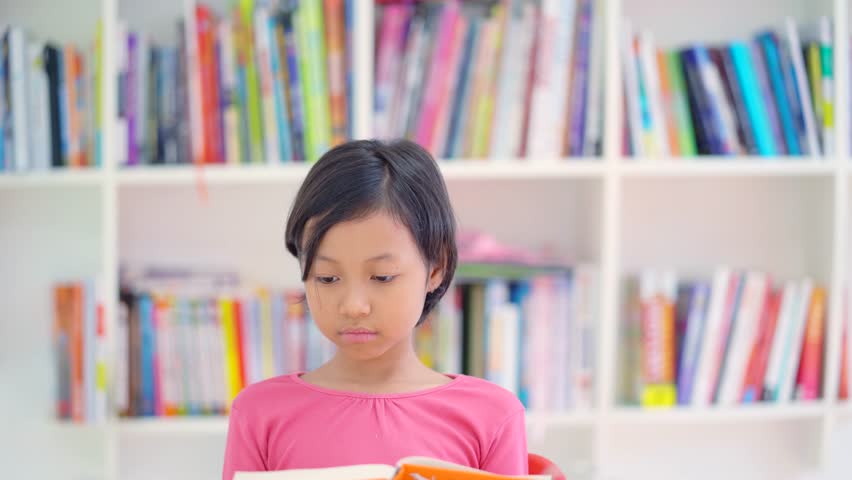 Little girl studying in the library while reading a book on the table. Shot in 4k resolution