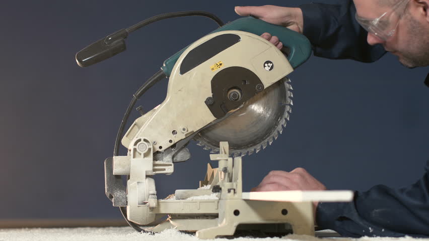 Worker in overalls on blue background cuts out 4K wood item on the electric saw. stream of sawdust from the machine tool when processing tree. When processing bar, large amount of chips is deposited.