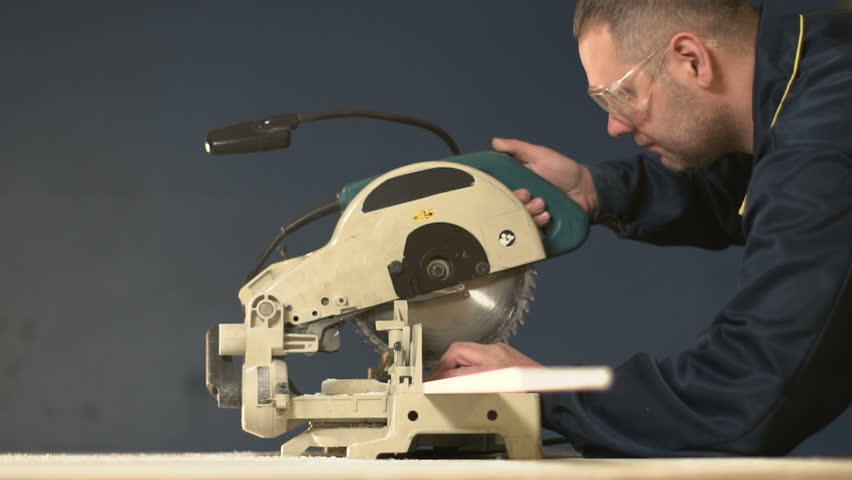 worker in overalls on blue background cuts out slow motion wood item on electric saw. stream of sawdust from machine tool when processing tree. When processing bar, large amount of chips is deposited.