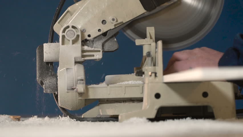 Worker in overalls on blue background closeup slow motion wood item on electric saw. When processing bar, large amount of chips is deposited. stream of sawdust from machine tool when processing tree.