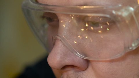A close-up adult young man at the factory looks at his work. The sparks from a man reflect sparks from welding slow motion. The guy's eyes are close-up with glasses looking at the welding slow mo.