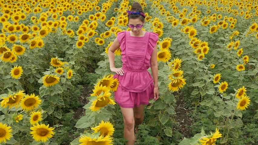girl in pink dress walking on the field with sunflowers