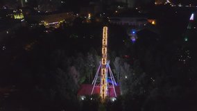 Amusement Park Aerial Shot Night City Lights. Clip. Aerial view moving front of beautiful Ferris wheel in the background lighting up the summer night