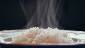 Jasmine rice in a white ceramic plate with smoke floating, background is black, suitable for cooking menu.
