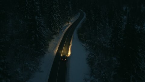 Aerial shot of cars driving through a snowy forest at night.